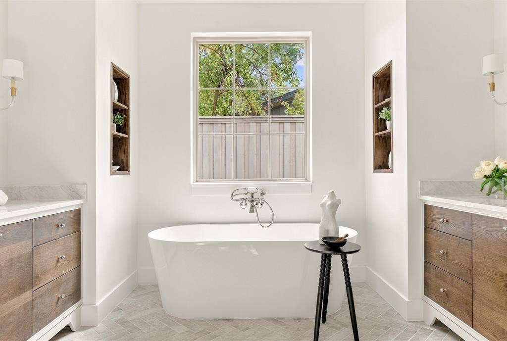 4953 Forest Bend Road, Dallas, TX 75244 Freestanding soaking tub with wall-mounted plumbing fixtures, wood-finish cabinetry, herringbone-patterned tile flooring, and integrated wall shelving