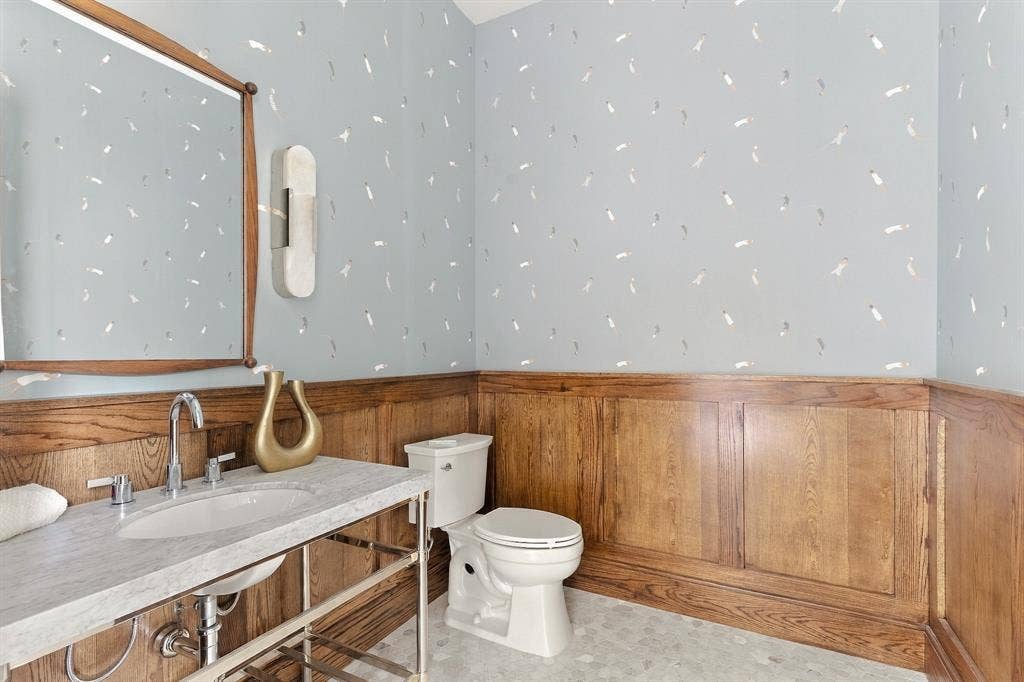 4953 Forest Bend Road, Dallas, TX 75244 Custom wood wainscoting, light-toned stone-finish vanity top, polished metal washstand, patterned wallpaper, and chrome wall-mounted light fixture