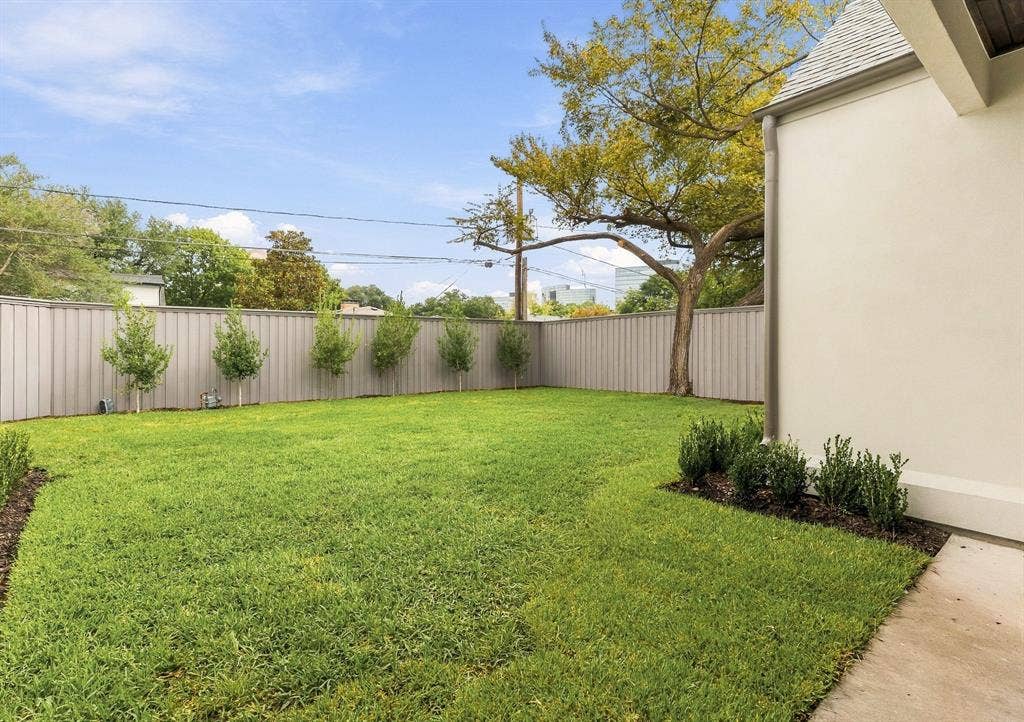 4953 Forest Bend Road, Dallas, TX 75244 Backyard featuring a grass lawn, perimeter metal fencing, mature trees, and landscaped garden beds