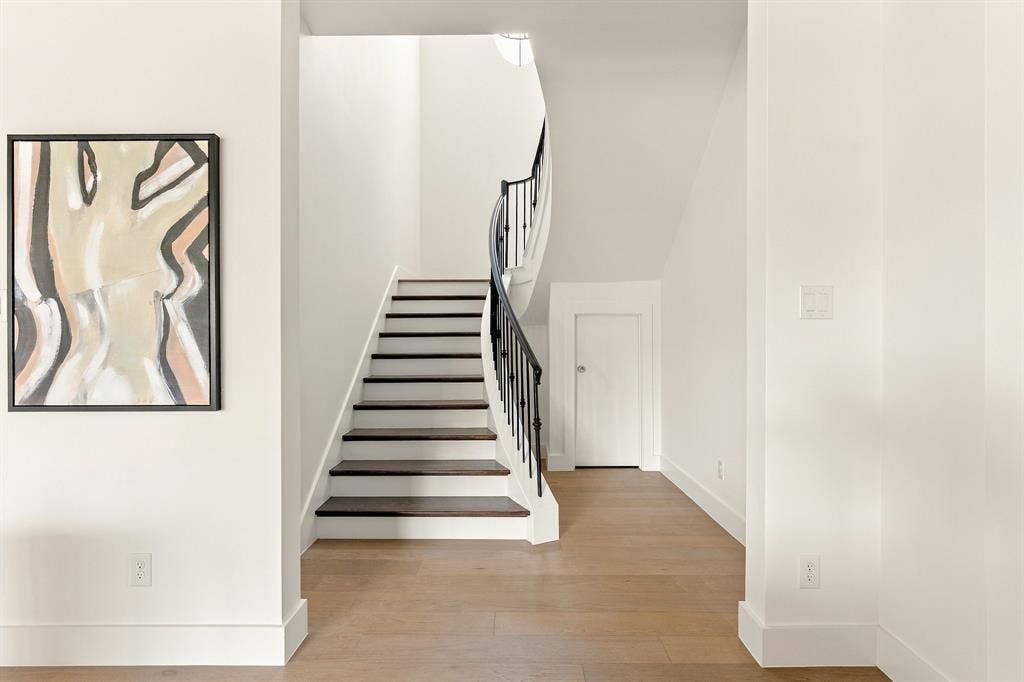 4953 Forest Bend Road, Dallas, TX 75244 Staircase featuring dark-toned wood treads, white risers, and a wrought-iron railing with a curved silhouette, set against wood-finish flooring
