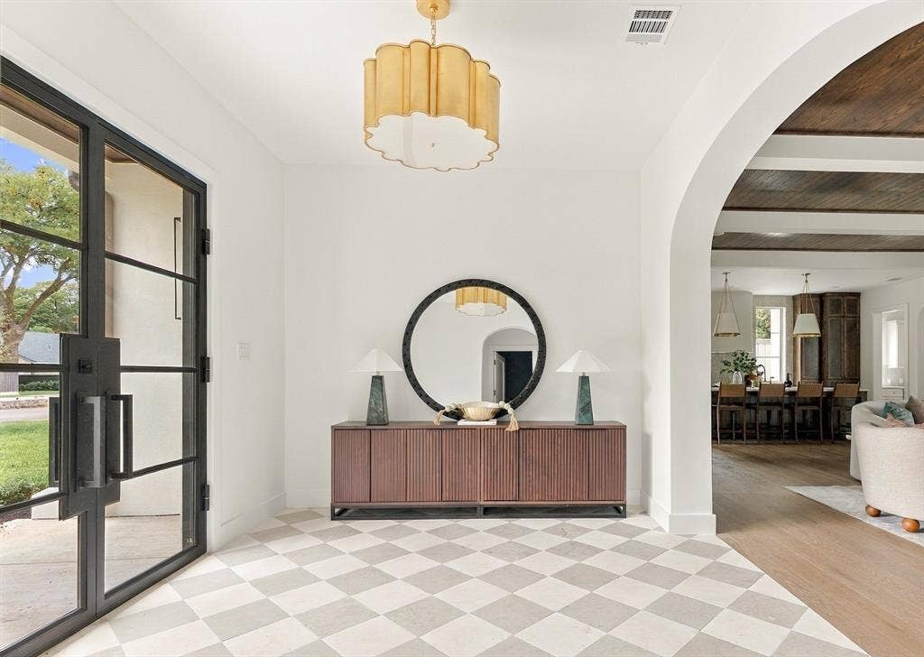 4953 Forest Bend Road, Dallas, TX 75244 Foyer featuring checkered stone flooring, a decorative gold-tone pendant light, black-framed glass entry door, and a prominent arched entryway