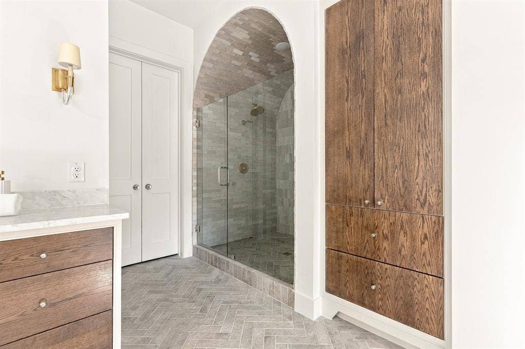 4953 Forest Bend Road, Dallas, TX 75244 Walk-in shower featuring an arched brick ceiling, stone tile surround, and frameless glass door, paired with custom wood-finish built-in cabinetry, stone-top vanity, and herringbone tile flooring