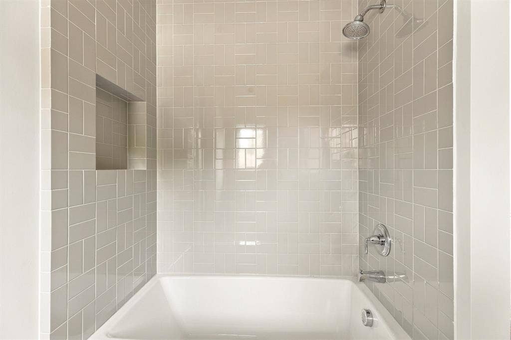 4953 Forest Bend Road, Dallas, TX 75244 Shower and tub combination featuring neutral ceramic subway tile in a herringbone pattern, a built-in recessed niche, and polished chrome fixtures