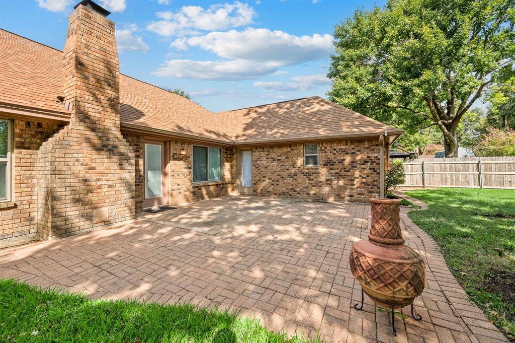 339 Park North Lane, Keller, TX 76248 Rear exterior featuring a brick facade, chimney, herringbone-patterned paved patio, and perimeter wood fencing