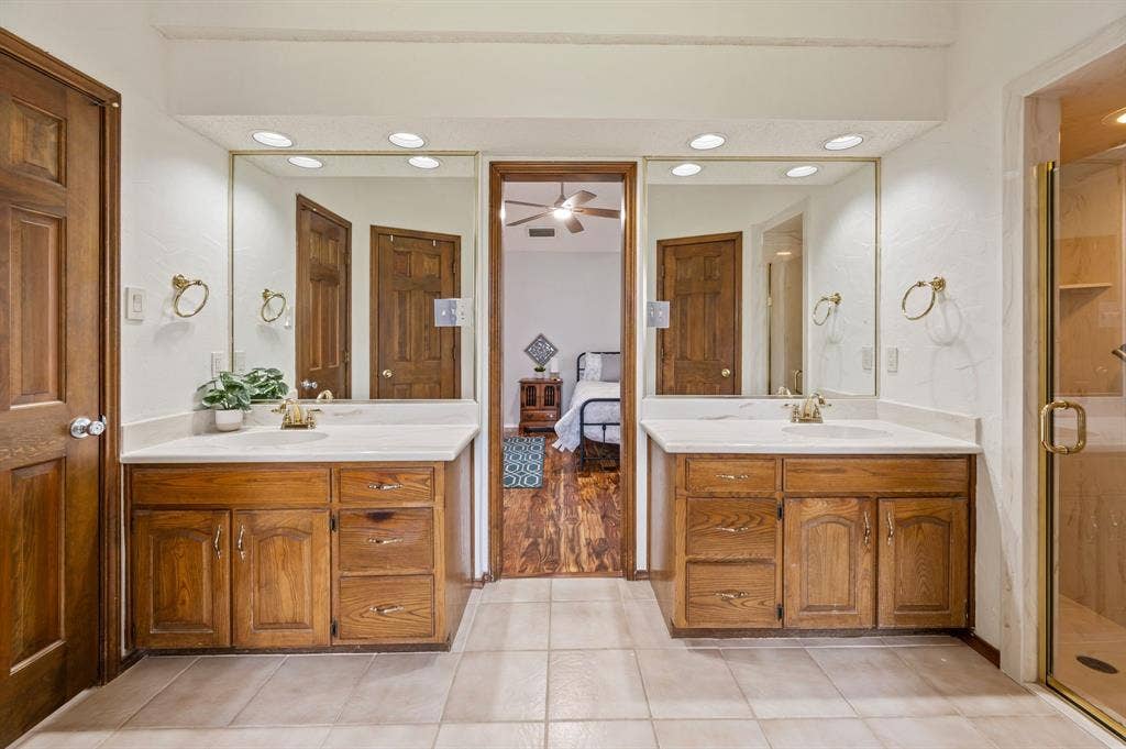 339 Park North Lane, Keller, TX 76248 Dual-vanity bathroom featuring solid-wood cabinetry, stone-finish countertops, recessed lighting, and a glass-enclosed shower with gold-tone hardware