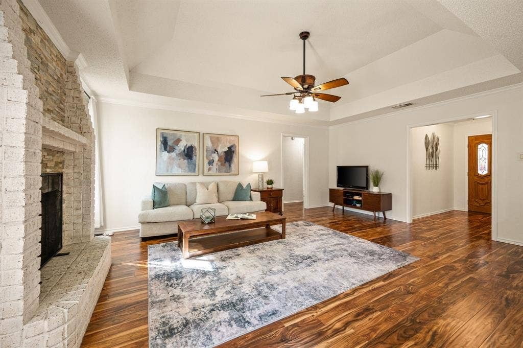339 Park North Lane, Keller, TX 76248 Living area featuring a floor-to-ceiling brick fireplace with stone accents, tray ceilings, wood-finish flooring, and a multi-light ceiling fan