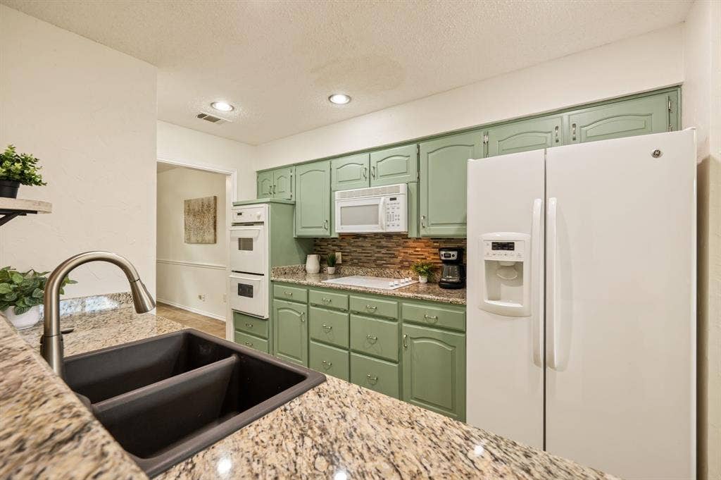 339 Park North Lane, Keller, TX 76248 Kitchen featuring sage-toned cabinetry, multi-tonal stone backsplash, speckled stone-finish countertops, built-in dual wall oven, and a double-basin undermount sink with a gooseneck faucet