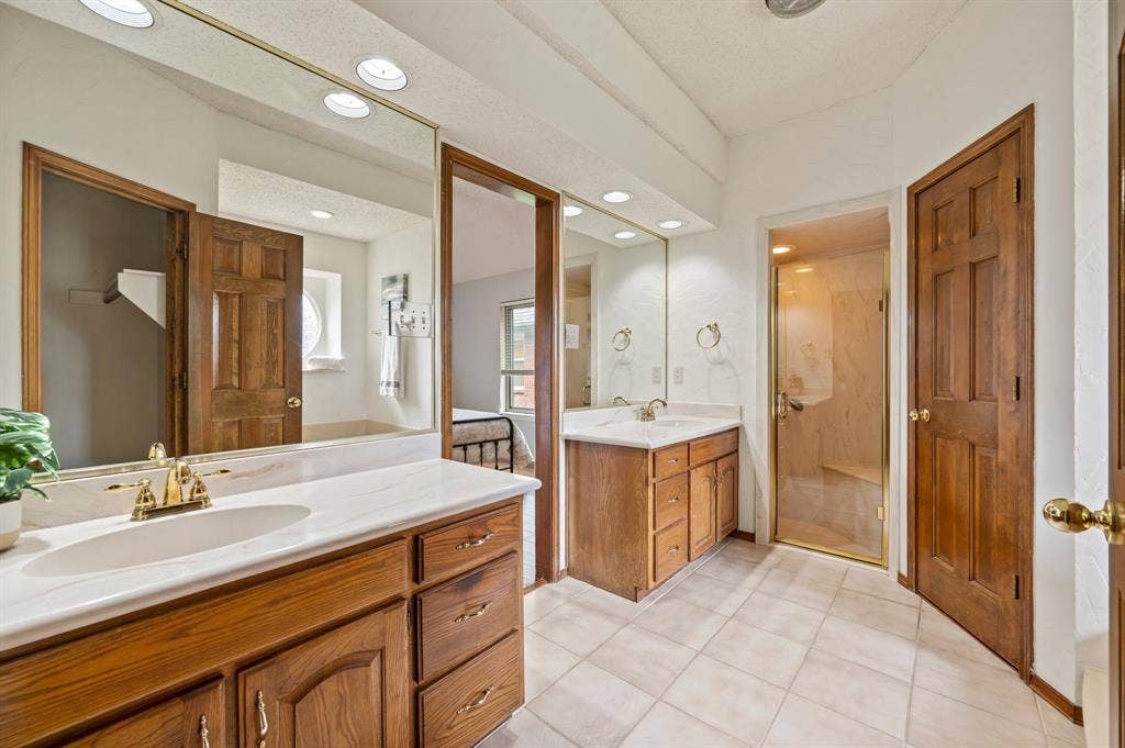 339 Park North Lane, Keller, TX 76248 Dual-vanity cabinetry with wood finish, large wall-mounted mirrors, recessed lighting, tile flooring, and enclosed shower with glass door