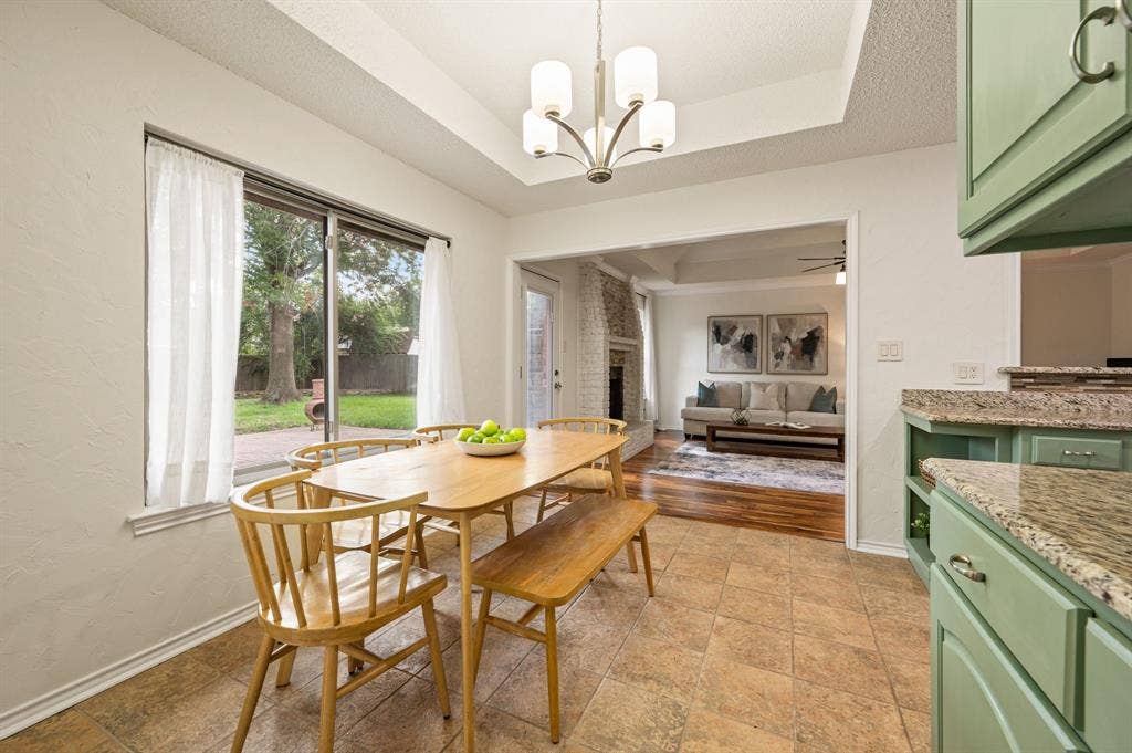 339 Park North Lane, Keller, TX 76248 Dining area featuring a tray ceiling with a multi-arm chandelier, light-toned tile flooring, sage green cabinetry with stone-finish countertops, and sliding glass doors