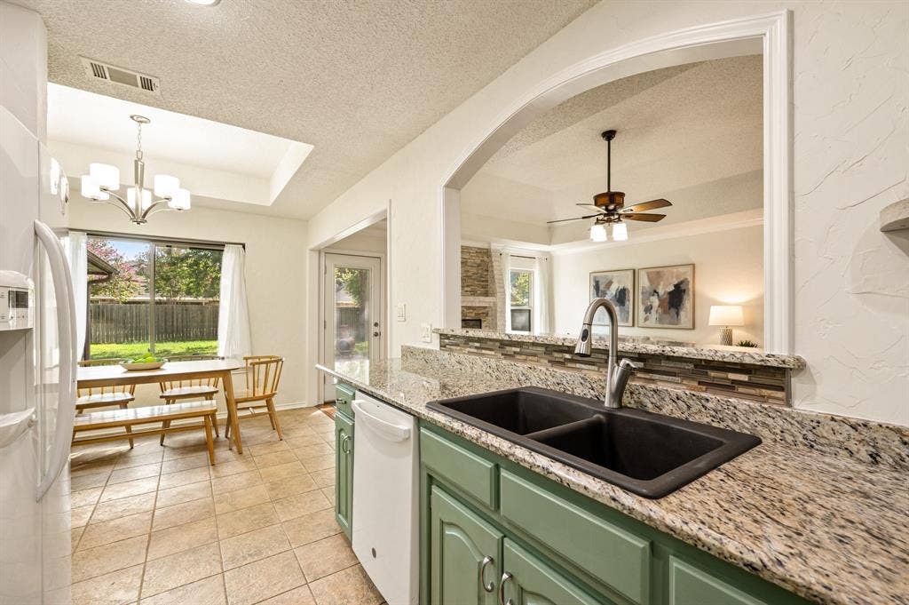 339 Park North Lane, Keller, TX 76248 Kitchen featuring stone-finish countertops, a double-basin undermount sink with a gooseneck faucet, tile flooring, and a pass-through window with a decorative tiled backsplash