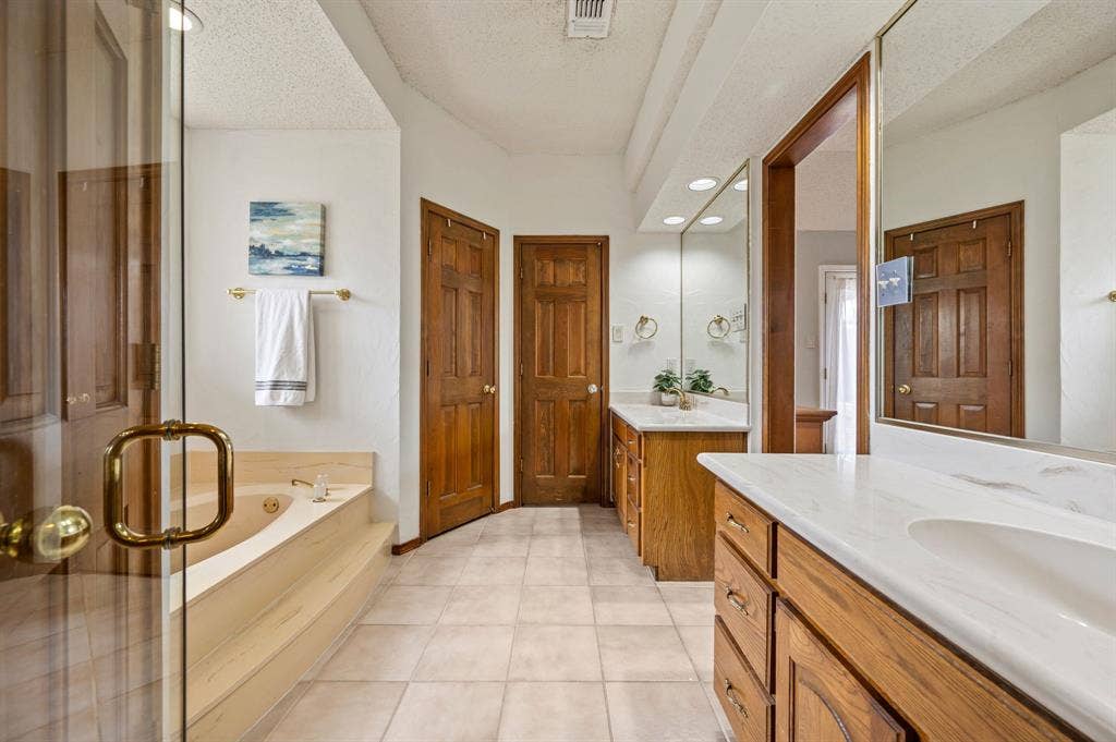 339 Park North Lane, Keller, TX 76248 Bathroom featuring dual wood-finish cabinetry, solid-surface countertops, integrated sinks, a drop-in soaking tub, and tile flooring