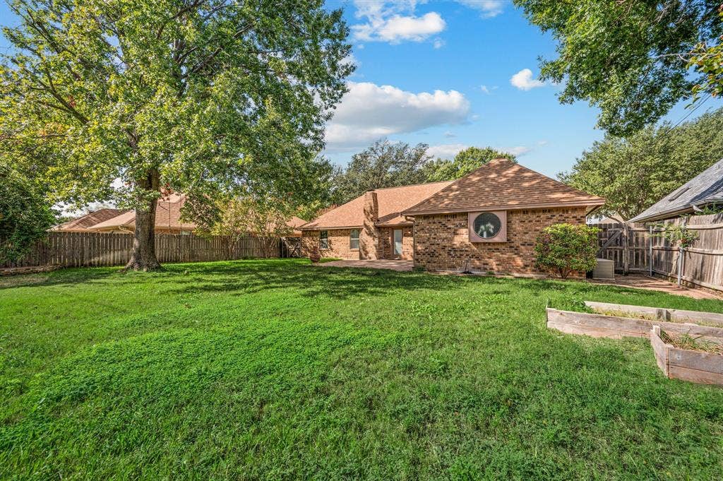 339 Park North Lane, Keller, TX 76248 Expansive backyard featuring a brick exterior, mature trees, a circular accent window, and raised wooden planting beds
