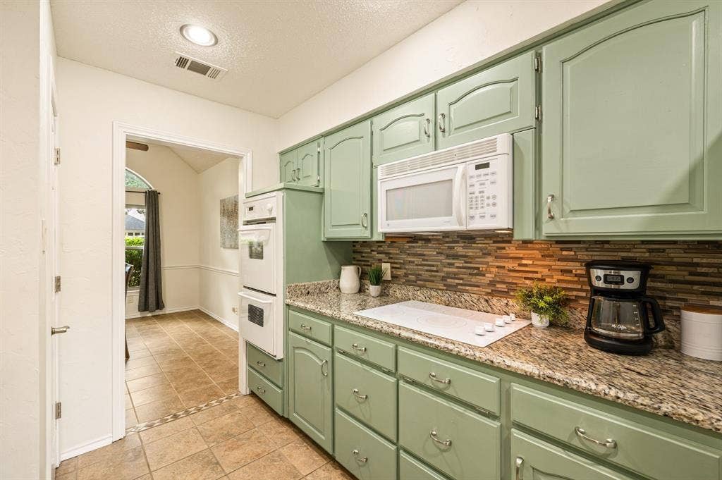 339 Park North Lane, Keller, TX 76248 Kitchen featuring sage green cabinetry, stone-patterned countertops, mosaic tile backsplash, white built-in double wall oven, and white electric cooktop