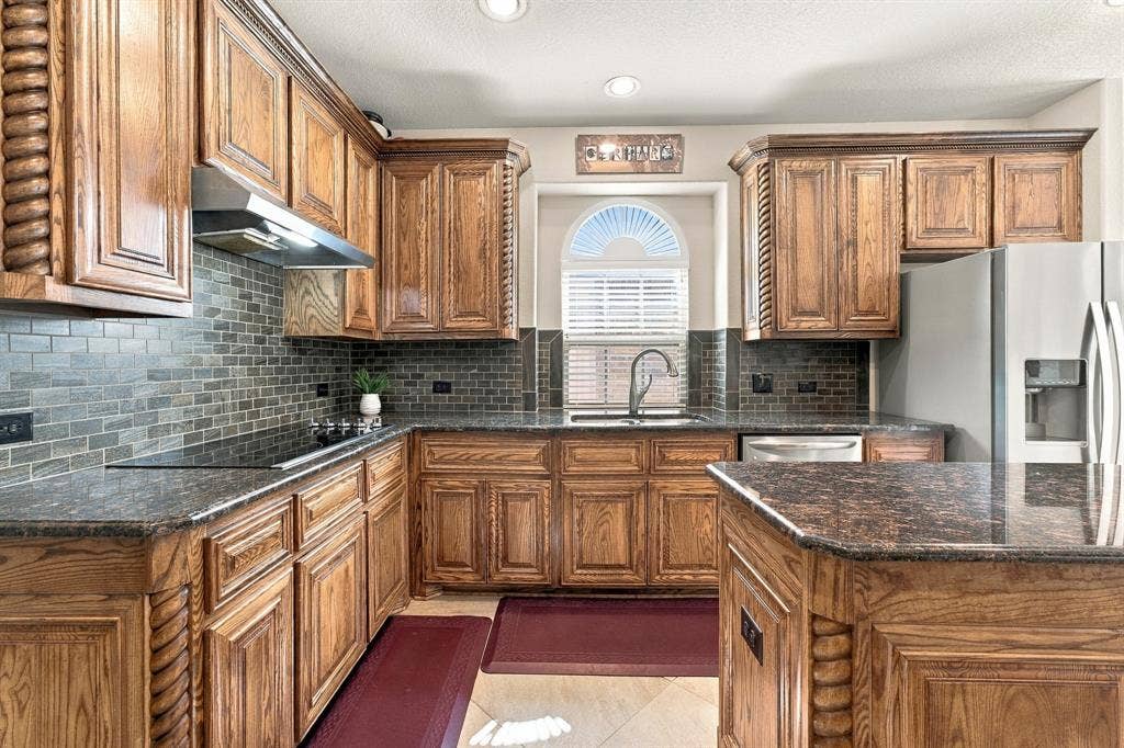 Kitchen featuring raised-panel wood cabinetry with decorative rope detailing, stone countertops, a tiled backsplash, and an arched window