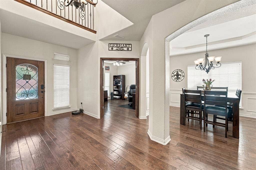 Foyer featuring wood-finish flooring, a two-story ceiling, a wrought-iron staircase railing, a decorative wood-paneled front door with glass insert, and arched entryways