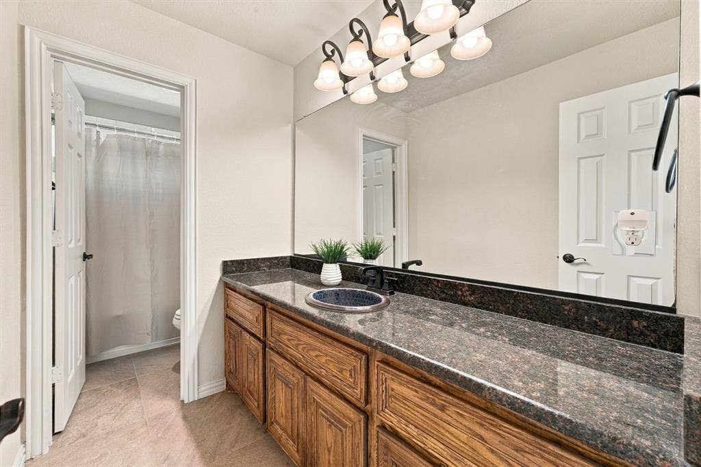 Bathroom featuring a stone-finish countertop, oval undermount sink, multi-drawer wood cabinetry, large vanity mirror, and multi-bulb light fixture