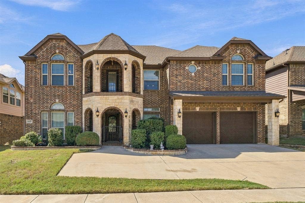 Multi-level brick exterior featuring natural stone accents, a covered dual-level arched entryway, arched window detailing, and an attached two-car garage