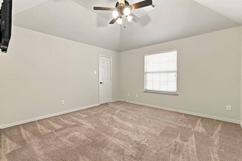 Vaulted ceiling featuring a central multi-blade ceiling fan with integrated light fixture, neutral wall palette, wall-to-wall carpeting, and a single-pane window with horizontal blinds