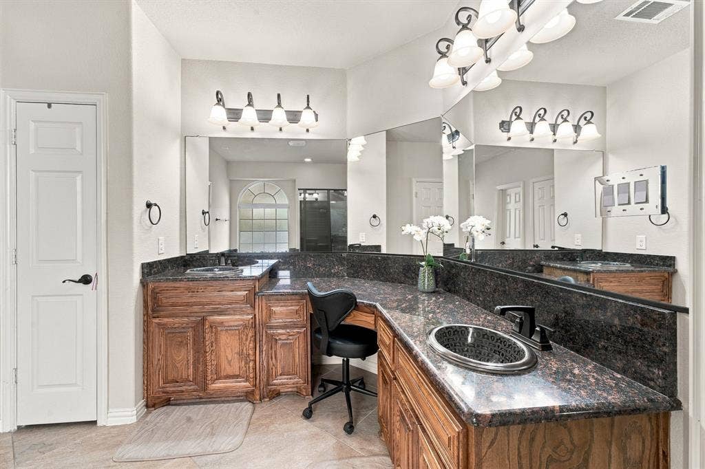 Dual-sink vanity featuring stained wood cabinetry, stone countertops, integrated oval basins, and wall-mounted light fixtures