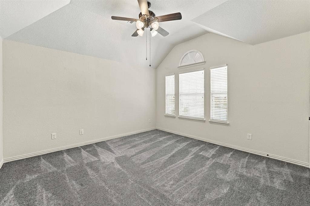 Vaulted ceilings, neutral wall color, wall-to-wall carpeting, ceiling fan with light kit, and multi-pane windows with arched transom detail