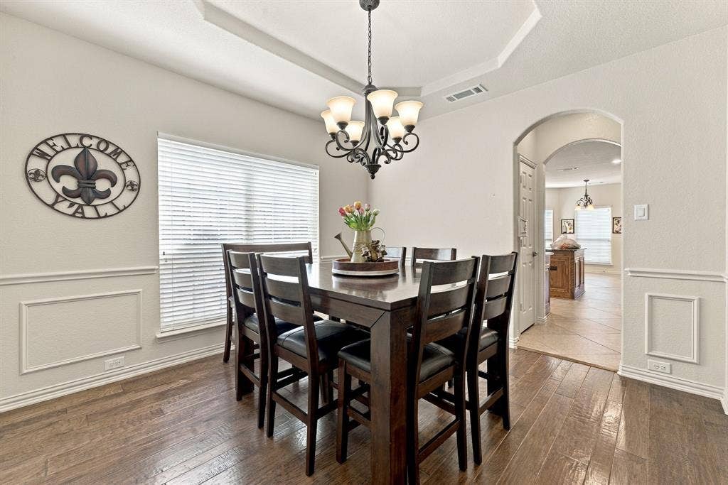 Dining area featuring wood-finish flooring, wainscoting, an arched entryway, and a tiered tray ceiling with a multi-arm chandelier