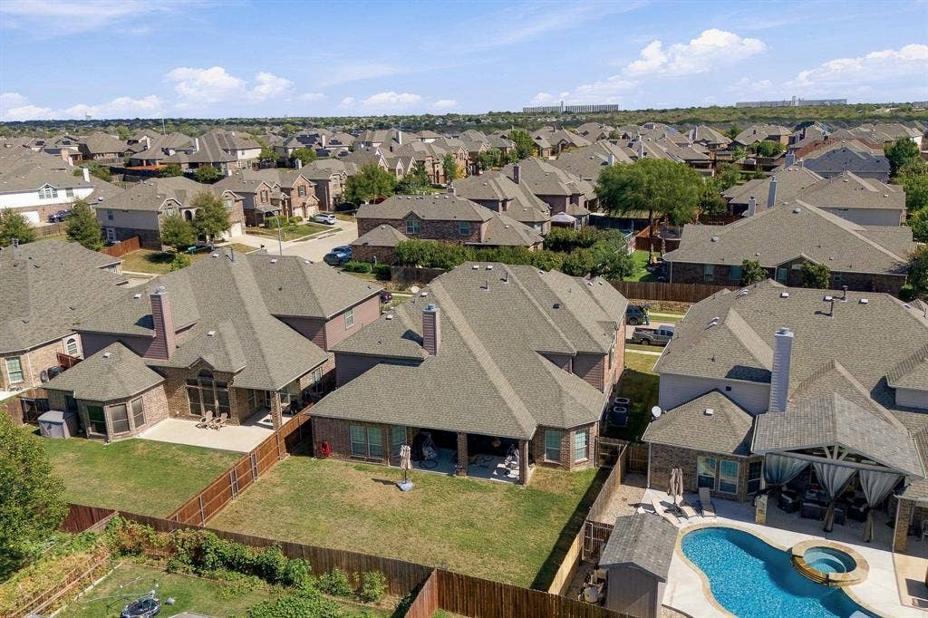 Aerial perspective of the residential property featuring a masonry exterior, a multi-pitched composition shingle roof, a covered patio, and a fenced backyard