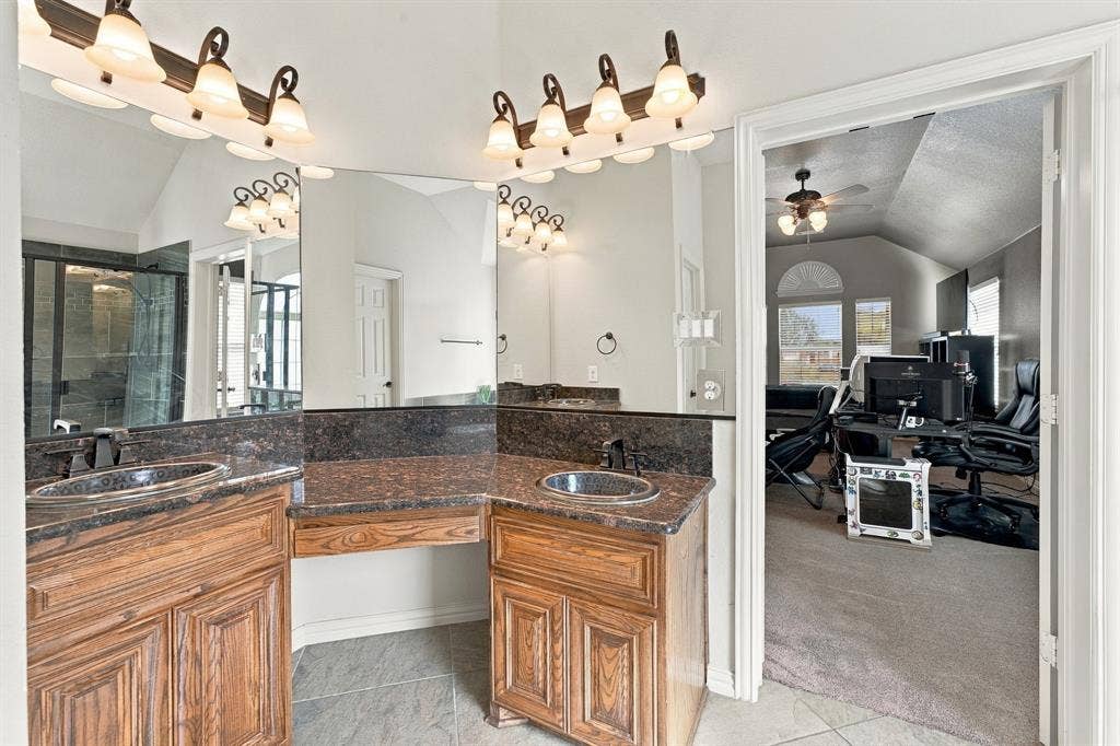 Dual-sink vanity featuring stone countertops, integrated oval basins, dark-finish cabinetry, full-width wall mirror, and two multi-light overhead fixtures