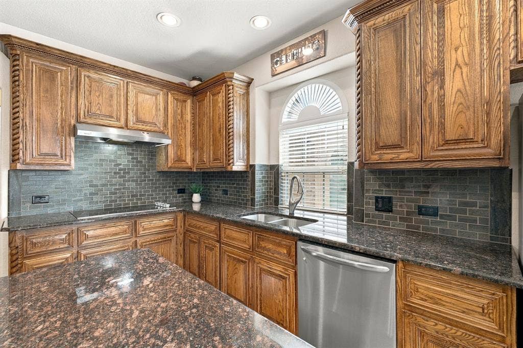 Kitchen featuring custom stained-wood cabinetry with rope detailing, dark stone countertops, stainless steel appliances, a subway-style tile backsplash, and an arched window