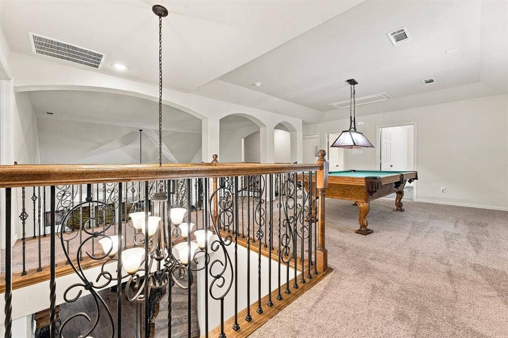 Open landing featuring decorative wrought-iron balusters with a wood handrail, vaulted ceilings, arched architectural detailing, and a multi-tiered chandelier
