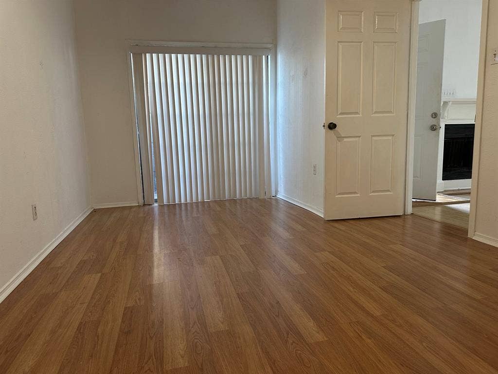 5757 E University Boulevard, #27p, Dallas, TX 75206 Room featuring wood-finish flooring, a white six-panel door, and floor-to-ceiling vertical blinds