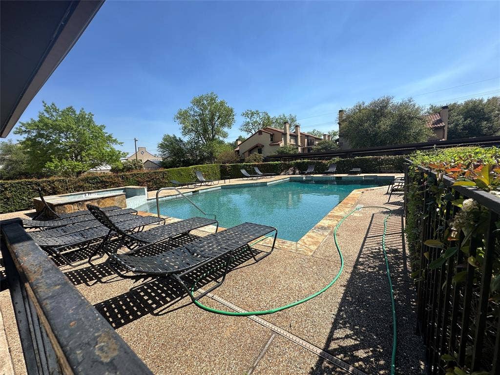 5757 E University Boulevard, #27p, Dallas, TX 75206 In-ground swimming pool with stone-tiled perimeter and integrated spa, set within a paved deck area bordered by manicured hedging and black metal fencing