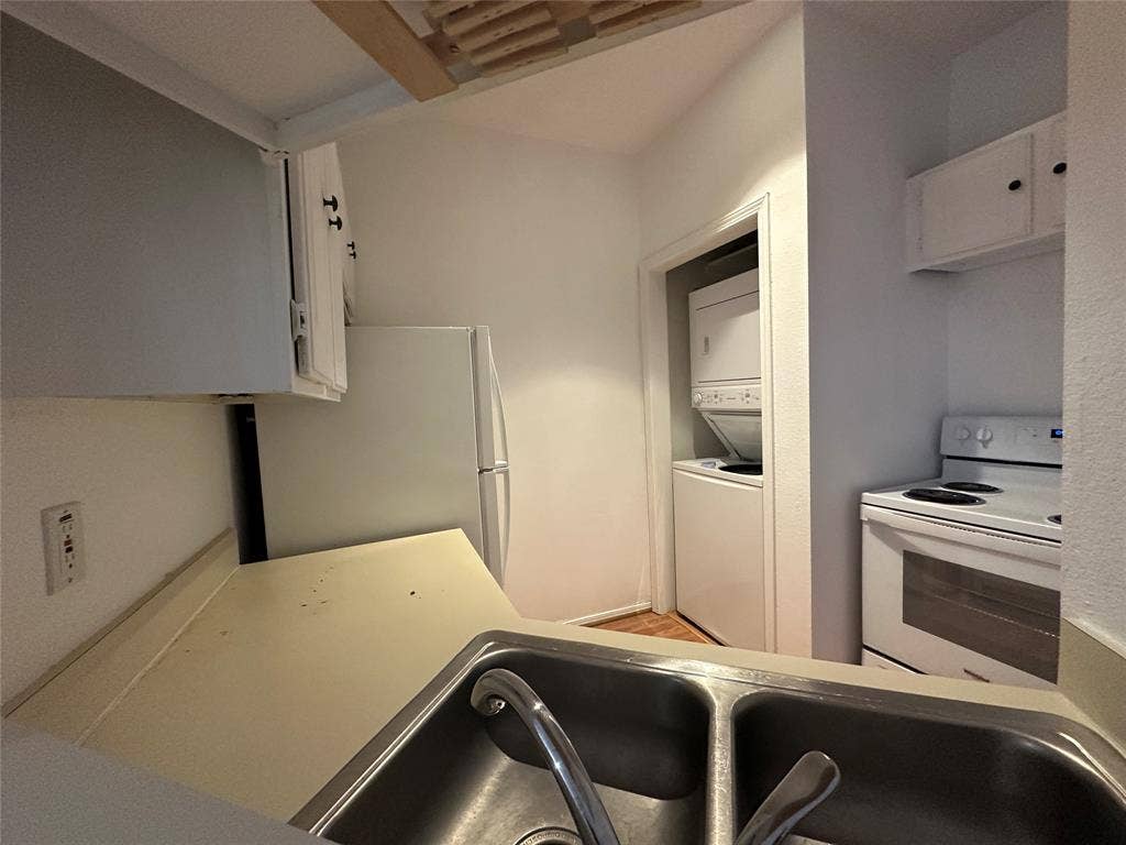 5757 E University Boulevard, #27p, Dallas, TX 75206 Kitchen featuring solid-surface countertops, dual-basin stainless steel sink, built-in white cabinetry, electric range, and integrated laundry closet with stacked washer and dryer