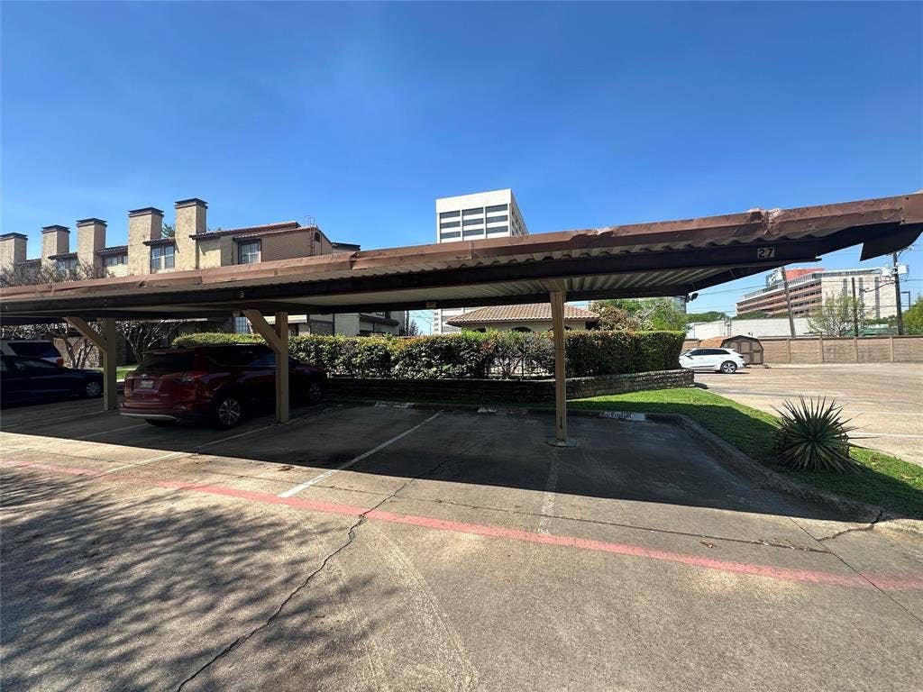 5757 E University Boulevard, #27p, Dallas, TX 75206 Covered parking area featuring a metal roof structure, concrete surfacing, and lined individual spaces