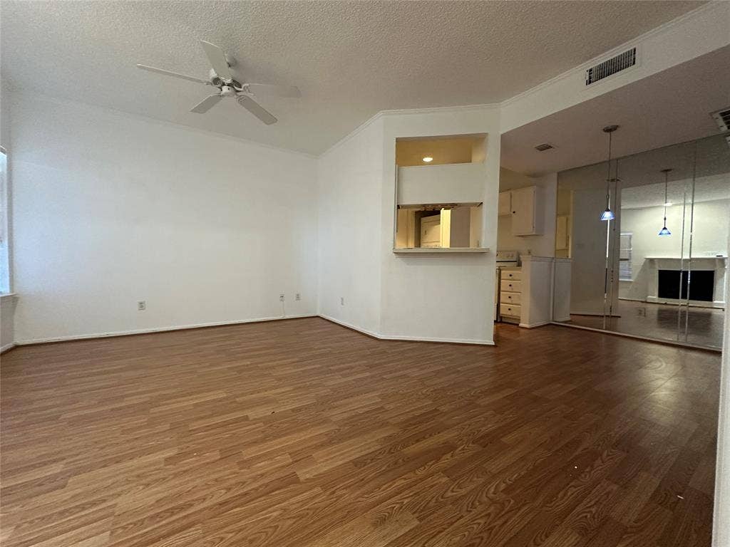 5757 E University Boulevard, #27p, Dallas, TX 75206 Open-concept room featuring wood-finish flooring, ceiling fan, pass-through window to the kitchen, and floor-to-ceiling mirrored closet doors