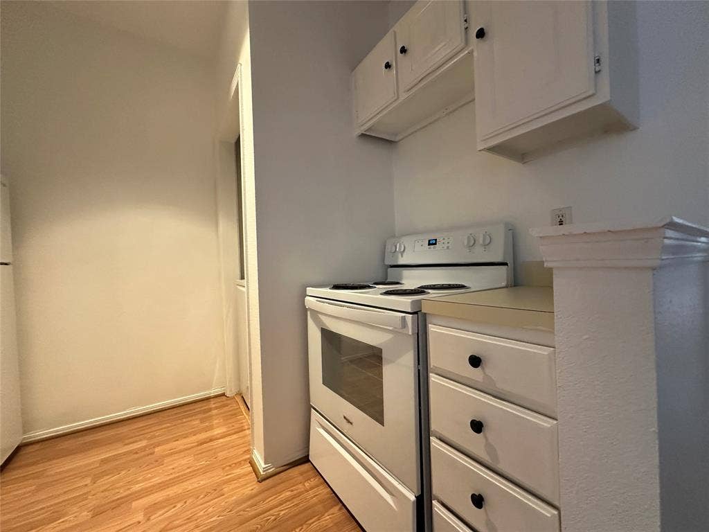 5757 E University Boulevard, #27p, Dallas, TX 75206 Kitchen area featuring white cabinetry with dark hardware, solid surface countertops, white freestanding electric range, and wood-finish flooring