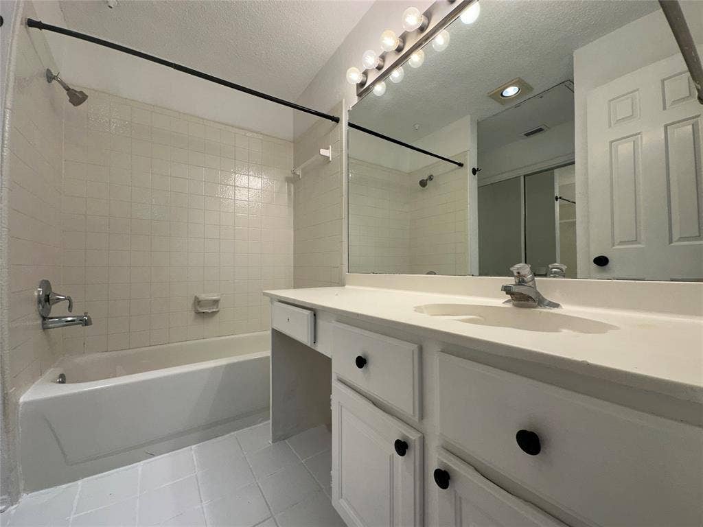 5757 E University Boulevard, #27p, Dallas, TX 75206 Bathroom featuring a vanity with white cabinetry, a single integrated sink, a large wall-mounted mirror with multi-bulb lighting, and a combination tub and shower with tile surround
