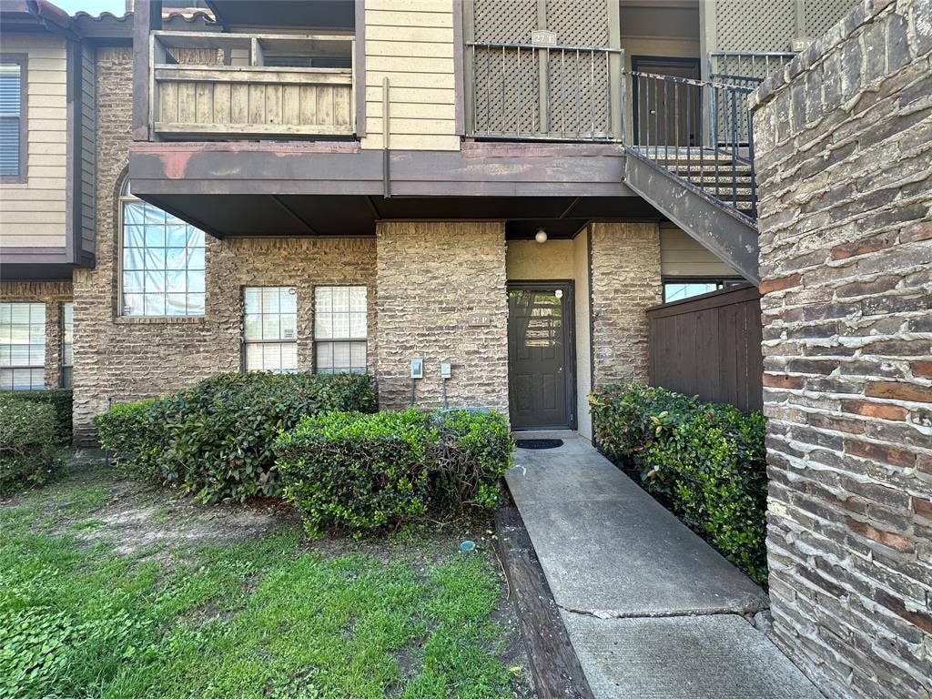 5757 E University Boulevard, #27p, Dallas, TX 75206 Multi-level exterior featuring textured stone masonry, horizontal siding, elevated balcony with lattice screening, and a private concrete walkway leading to the entrance