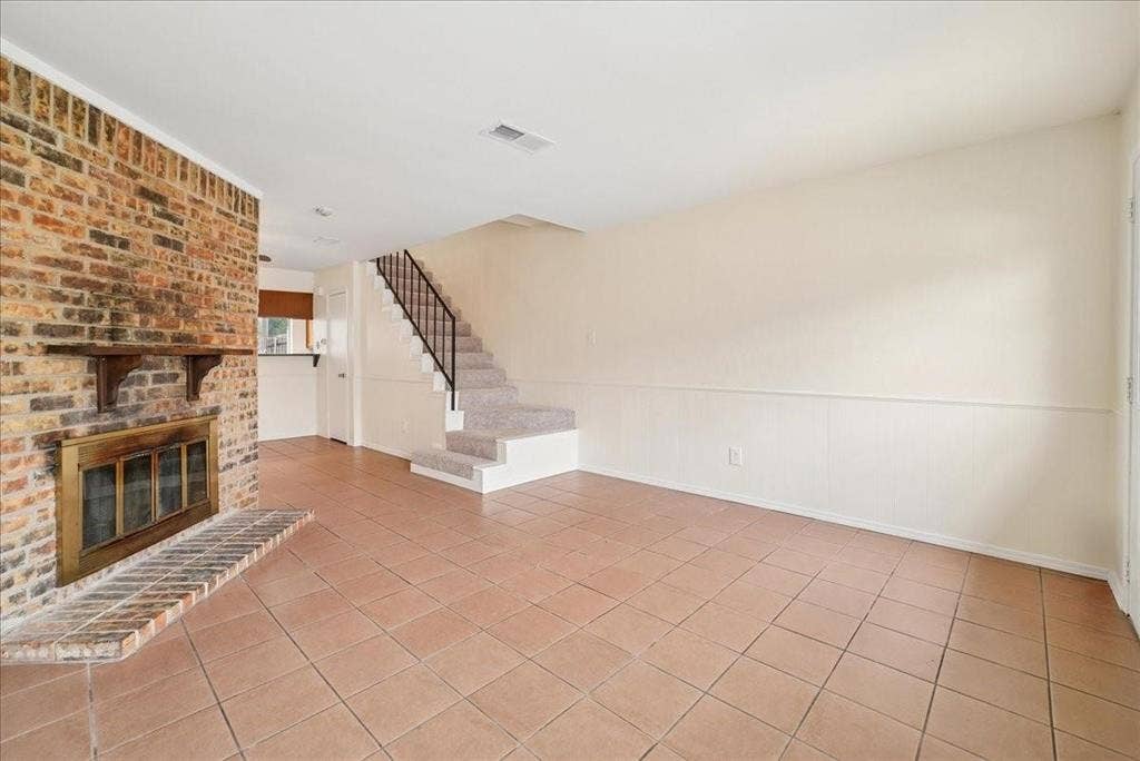 703 Lee Street, #6, Mesquite, TX 75149 Full-height brick fireplace featuring a wood mantel and tiled hearth, ceramic tile flooring, staircase with metal railing, and wainscoting