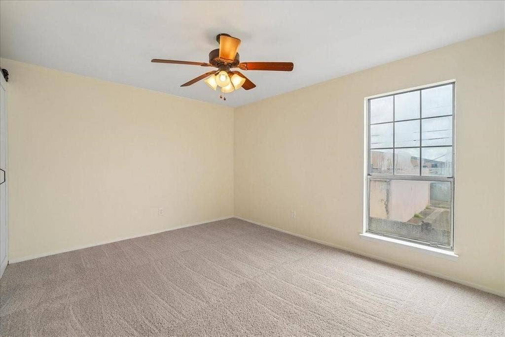 703 Lee Street, #6, Mesquite, TX 75149 Neutral-toned interior space featuring wall-to-wall carpeting, a multi-light ceiling fan, and a single-pane window with grid detailing