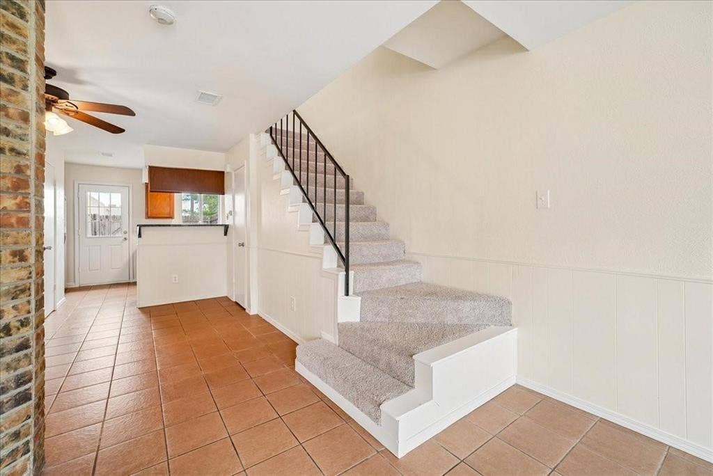 703 Lee Street, #6, Mesquite, TX 75149 Staircase featuring carpeted steps and a black metal railing, tile flooring, beadboard wainscoting, and a brick-finish accent pillar