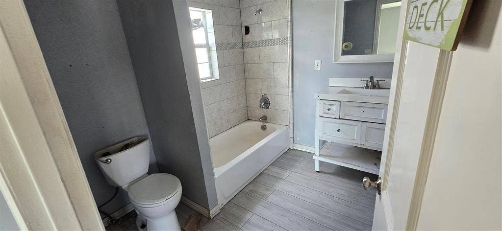 517 Clark Street, Garland, TX 75040 Bathroom featuring wood-finish flooring, a vanity with an integrated sink, a built-in tub with tile surround, and a wall-mounted mirror