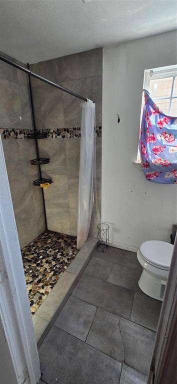 517 Clark Street, Garland, TX 75040 Walk-in shower featuring large-format neutral wall tile, a decorative stone-finish border, and a river-rock style pebble floor, complemented by large-format floor tiling and a standard white toilet