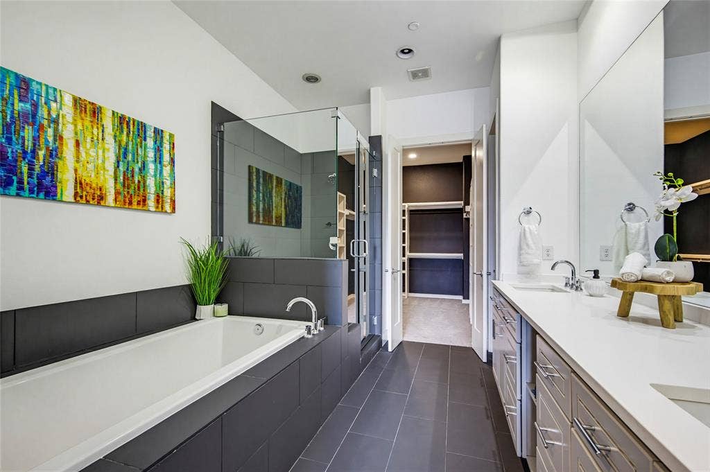 Bathroom featuring a dual-sink vanity with a quartz countertop, a deep soaking tub with tile surround, a glass-enclosed walk-in shower, and large-format tile flooring