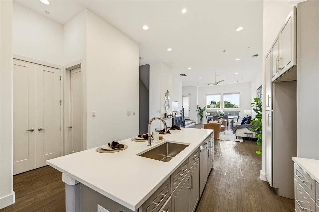 Kitchen island featuring a white countertop, stainless steel undermount sink, and high-arc faucet, complemented by grey cabinetry, recessed lighting, and wood-finish flooring