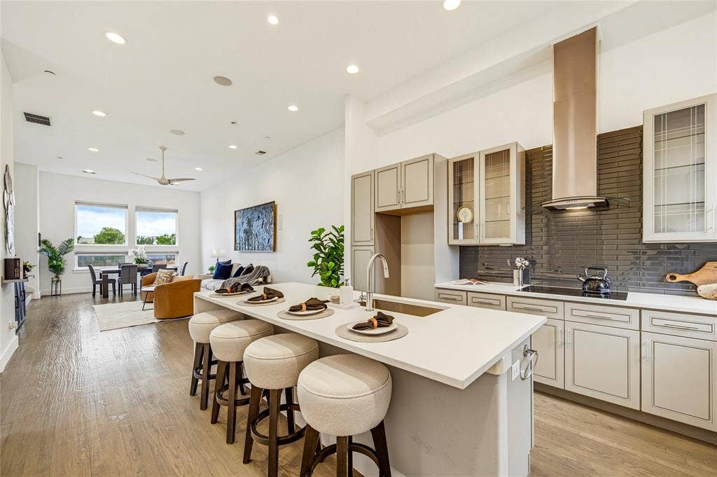 Kitchen featuring a quartz-topped island, light-toned cabinetry, a stainless steel range hood, dark tile backsplash, and wood-finish flooring