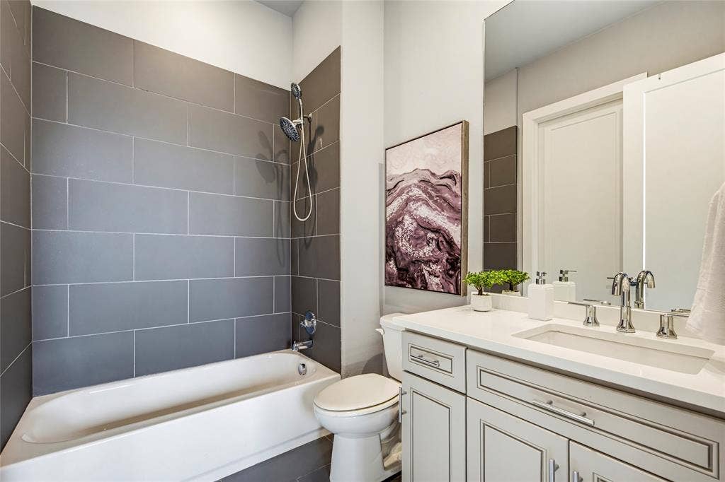 Bathroom featuring a large-format grey tile surround, a built-in tub, a vanity with a white countertop and undermount sink, and a full-height wall-mounted mirror