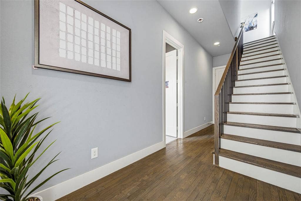 Staircase featuring wood-finish treads, white risers, and dark metal balusters, complemented by recessed lighting and wood-finish flooring