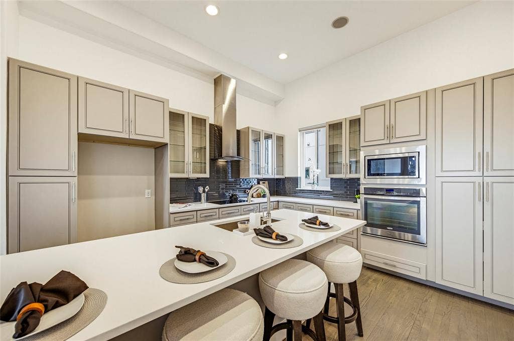 Kitchen featuring floor-to-ceiling cabinetry, a central island with a solid-surface countertop, stainless steel appliances, a chimney-style range hood, and wood-finish flooring