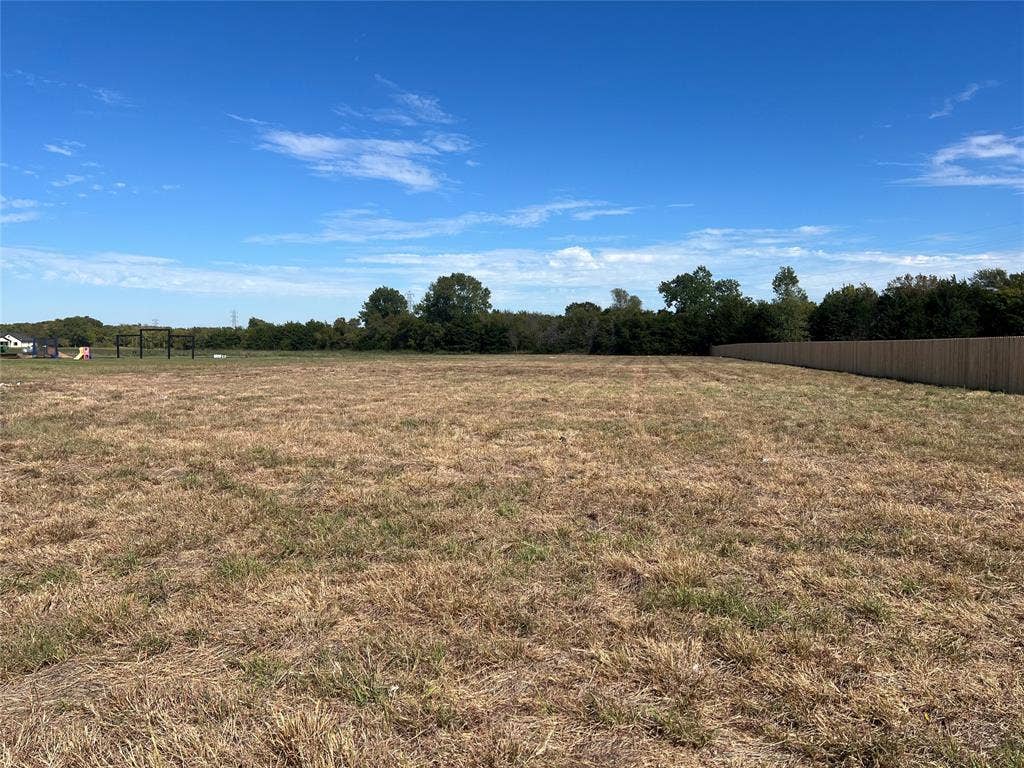 Expansive open lot featuring flat topography, a wood privacy fence, and mature perimeter trees