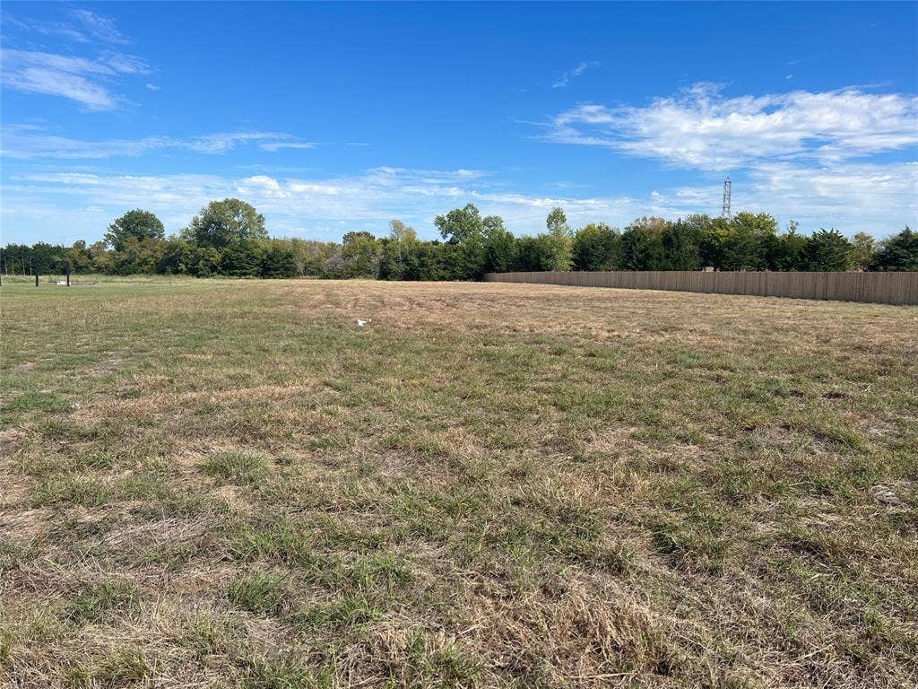 Expansive level lot featuring cleared acreage, perimeter wood fencing, and mature trees